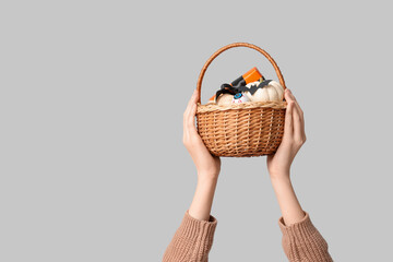 Wall Mural - Female hands with wicker basket of Halloween pumpkins and gift box on grey background