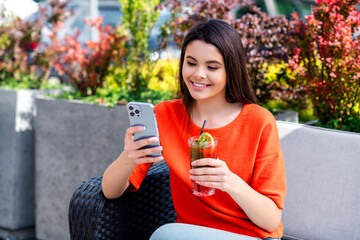 Sticker - Photo of attractive teen cheerful girl sit brench drink cocktail hold device wear red garment having fun outside outdoors