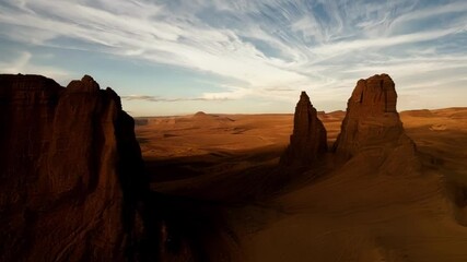 Poster - The sun sets over a desert landscape, casting long shadows on sandstone towers, with a dramatic sky painted in shades of orange, red, and brown