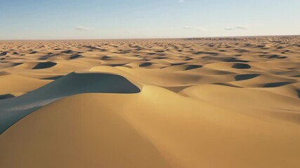 Poster - Aerial view of a vast desert landscape with sand dunes bathed in warm sunlight, creating a mesmerizing pattern of light and shadow