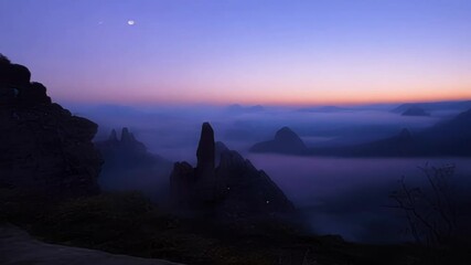 Poster - The last hues of twilight are fading from the sky as the moon shines over the peaks of a mountain range emerging from the fog