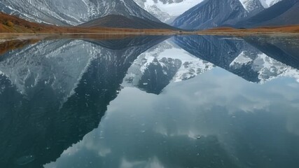 Aufkleber - Snow capped mountain peaks are reflecting in the still water of a lake, with clouds adding to the abstract effect of the scene