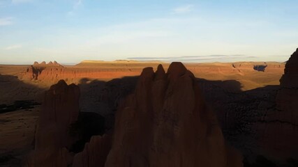 Poster - The warm glow of the setting sun bathes towering rock formations, casting long shadows across the vast and rugged desert landscape