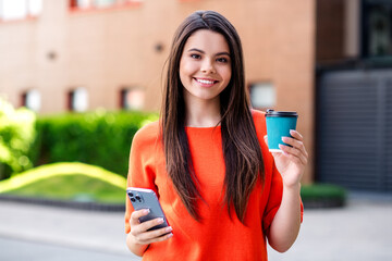 Sticker - Photo of positive teen adorable cheerful woman hold device coffee paper cup wear red outfit walk park sunny spring weather outside