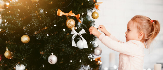 Wall Mural - Mother's helper. Little baby girl decorating Christmas tree at home, side view