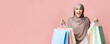© Prostock-studio - Shopaholic and seasonal sales concept. Excited arabian woman holding lot of bright shopping bags and credit card, looking to camera, pink background