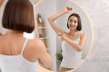 Sticker - Smiling woman applying roll-on deodorant near mirror at home, back view