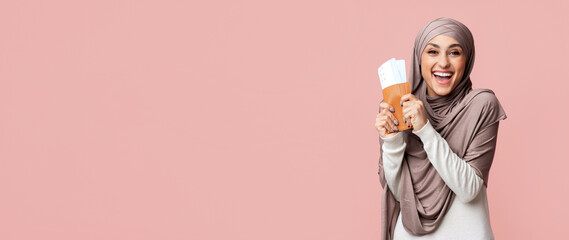 Muslim-friendly tourism concept. Excited arabic woman in hijab holding passport and boarding passes, ready to travel, pink background with free space