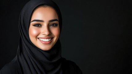 Beautiful young woman in a black hijab smiles against a black background.