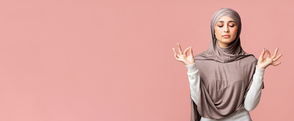 Zen. Relaxed muslim girl in hijab meditating with closed eyes, holding her fingers in mudra gesture over pink background with empty space