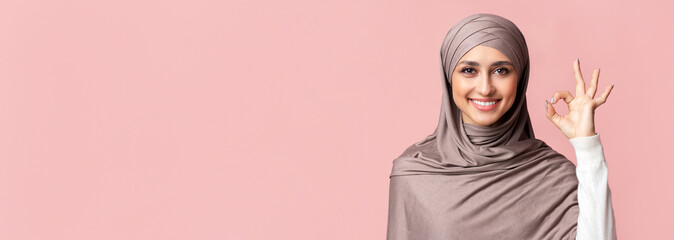 Wall Mural - Everything is ok. Happy islamic woman in hijab showing ok gesture over pink background in studio, free space