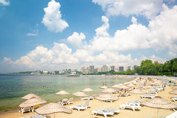 Istanbul, Turkey - July 7, 2024: People resting on the Caddebostan sandy beach. Citizens swimming and sunbathing under umbrellas on summer sunny day. Asian side of Istanbul city in the background