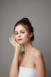 © SHOTPRIME STUDIO - Young woman in white dress posing with hand on face, looking at camera on gray background