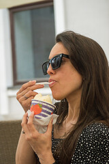 Latina woman eating ice cream in a glass with a spoon slowly enjoying the ice cream.