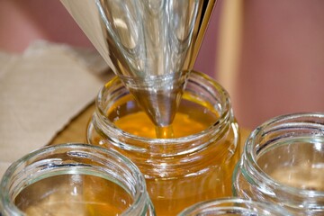 A detailed shot of honey being filled into a glass jar using a stainless steel funnel, showing the honey’s golden hue and the bottling process.