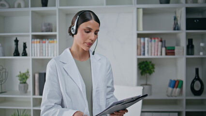 Serious doctor talking telemedicine consultation writing notes in clinic office.