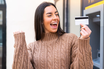 Young woman holding a credit card at outdoors celebrating a victory