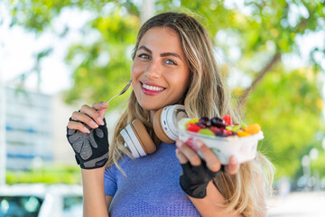 Canvas Print - Young blonde woman holding a bowl of fruit at outdoors