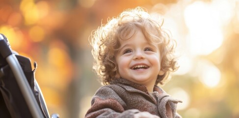 A joyful child with curly hair smiles brightly while seated in a stroller amidst a colorful autumn park in the golden hour