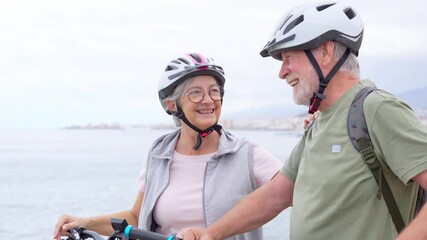 Wall Mural - Senior couple riding bikes together in rocky beach enjoying outdoor. Active mature people talking holding mountain bikes. Bicycle lifestyle concept, having fun
