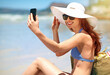 © ThurstanJam/peopleimages.com - Woman, smile and sunglasses on beach for selfie, tanning and travel in summer. Tourist, towel and happy on sand for photography, holiday and live streaming at ocean with peace and calm in Mauritius