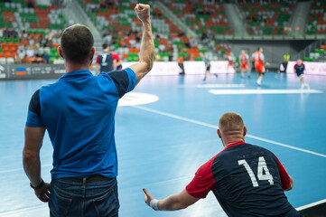 View form the behind on head coach and substitutions bench with handball match in background.