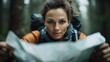 © familymedia - A female trekker in an orange jacket carefully examines a map in a wooded area, capturing the spirit of determination and careful planning in the great outdoors.