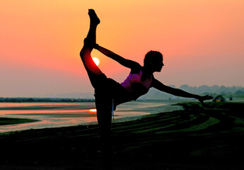 backlight silhouette of young and slim unrecognizable girl doing gymnastics on the seashore