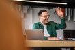 © Moon Safari - Portrait of young businessman laughing and waving away while working over laptop on desk in office