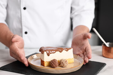 Professional chef with delicious cake at table in kitchen, closeup