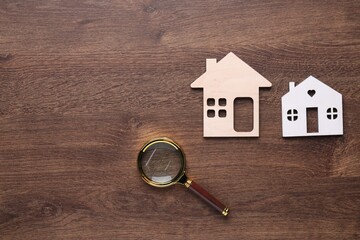 Wall Mural - House hunting. Magnifying glass and house figures on wooden background, flat lay. Space for text