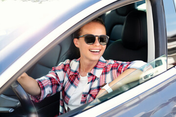 Cheerful young woman in sunglasses driving her new car, enjoying a summer road trip.