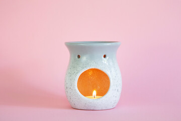 Aromatherapy grey oil burner with lit tea light candle against a pink pack background  