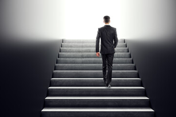 Businessman walking up concrete stairs towards a bright future, symbolizing growth and ambition.