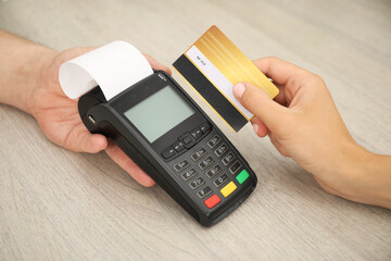 Canvas Print - Man taking payment from client via credit card terminal at wooden table, closeup