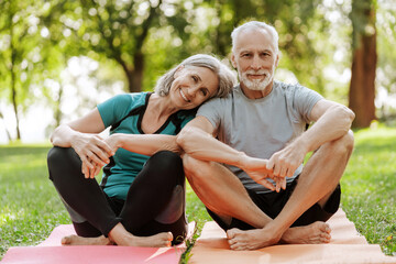 Senior couple relaxing on yoga mat in park after exercising together