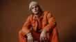 © The Little Hut - Fashionable guy in 20s in orange jumpsuit and jacket beige beanie posing on brown background : Generative AI