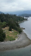 Wall Mural - A scenic ocean inlet with a rocky beach, forest, mountains, with cloudy skies in the background. British Columbia, Canada.