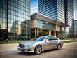 © Four888 - A sleek, silver luxury sedan is parked in front of a modern, glass-walled corporate headquarters building displaying a