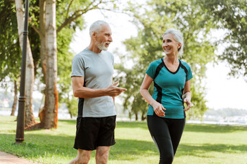 Wall Mural - Senior couple wearing sportswear walking and talking in the park