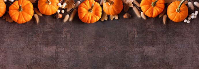 Poster - Fall top border of orange pumpkins, berries and natural autumn decor. Overhead view on a rustic dark stone banner background with copy space.