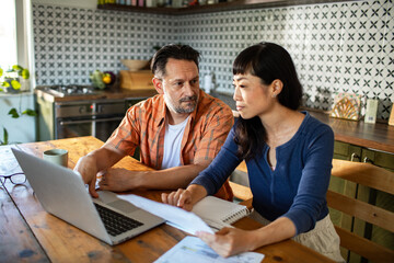 Couple reviewing documents together while using laptop at home