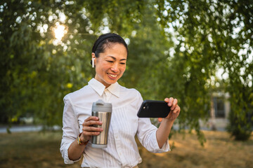 Wall Mural - Mature japanese woman watch funny videos on mobile phone in the park