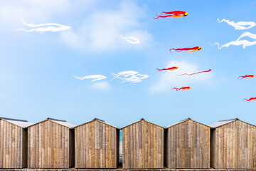 White and red kites flying in blue skies over beach cabins in Dieppe, France