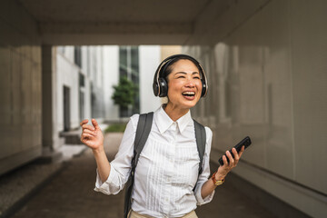 Wall Mural - japanese woman listen music on mobile phone between modern buildings