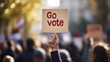 © capuchino009 - Empowering Community Participation - Close-Up of Hand Holding 'Go Vote' Sign at Rally for Voter Mobilization