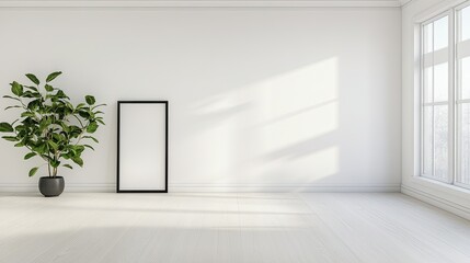 A blank black picture frame rests on the floor, leaning against an empty white wall in a bright room filled with natural light and greenery from large windows