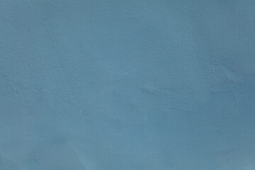 Blue or dark-blue wall, texture, background. The building wall, painted with water-based paint. Pale (flat) surface and backdrop in soft blue color. Flat surface with small dents and unevenness