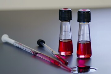 Poster - Two flasks containing red liquid are being analyzed by a scientist using pipettes in a laboratory setting