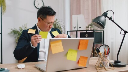 Wall Mural - Tired exhausted Asian businessman working on laptop at office with many sticker task inscriptions. Freelancer man busy occupation feels sad boredom overworked multitasking. Panic attack, deadline